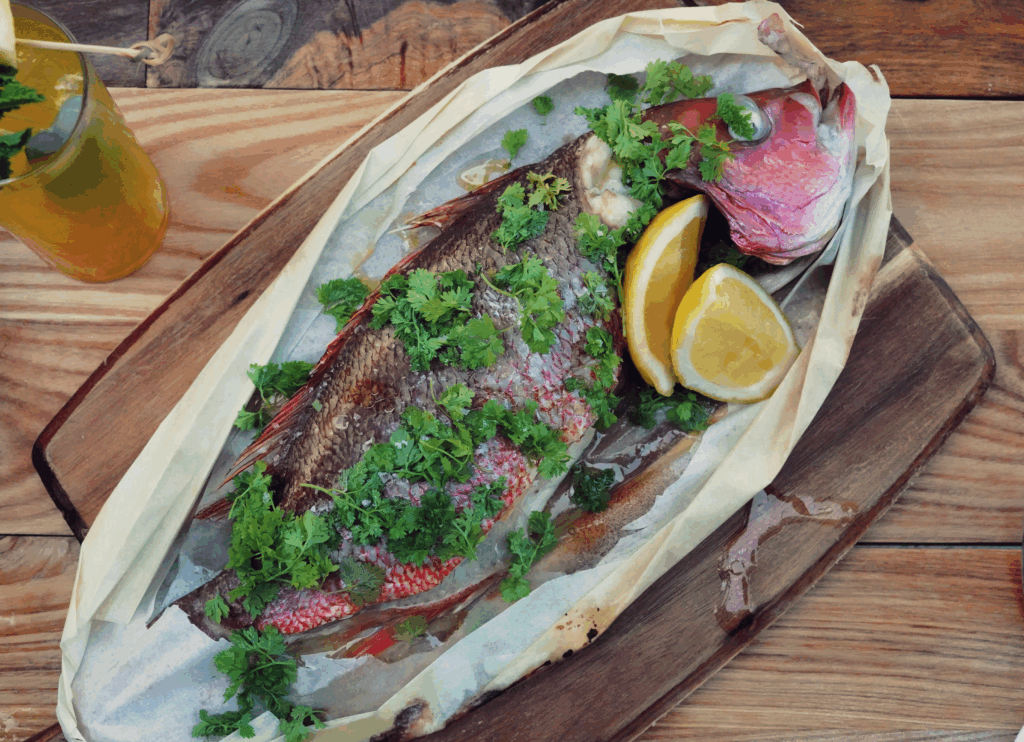 whole fish topped with fresh parsley and lemons on a wooden board