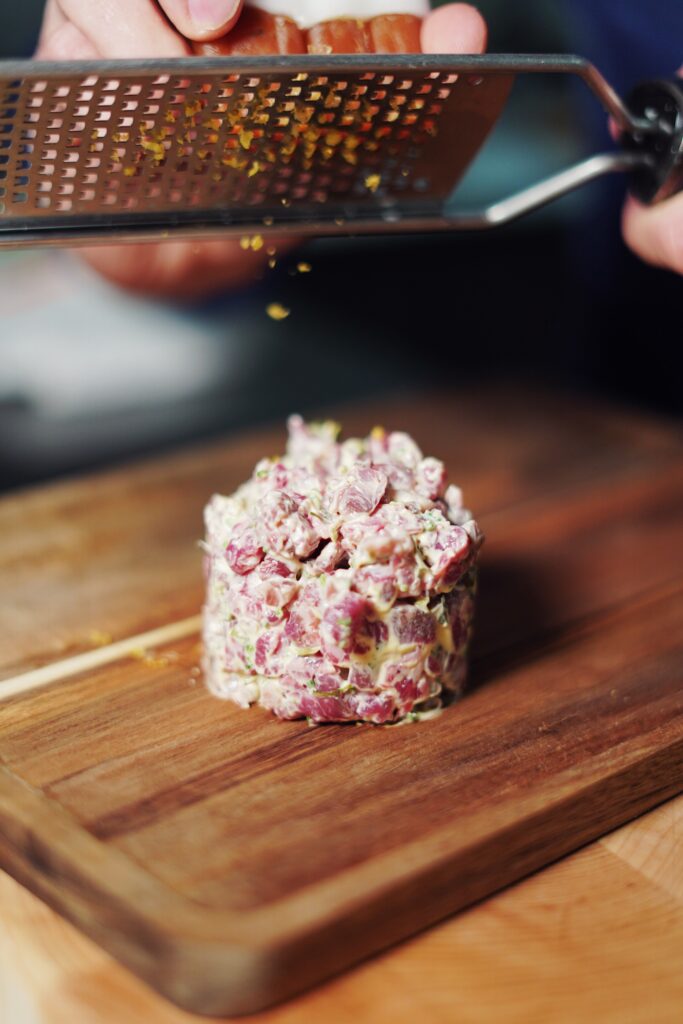 hands shaving citrus zest on top of beef tartare